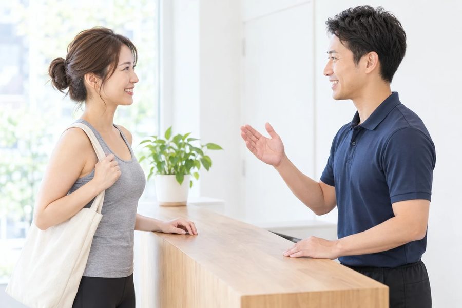 スタジオの受付でトレーナーが来店した女性を迎えている様子