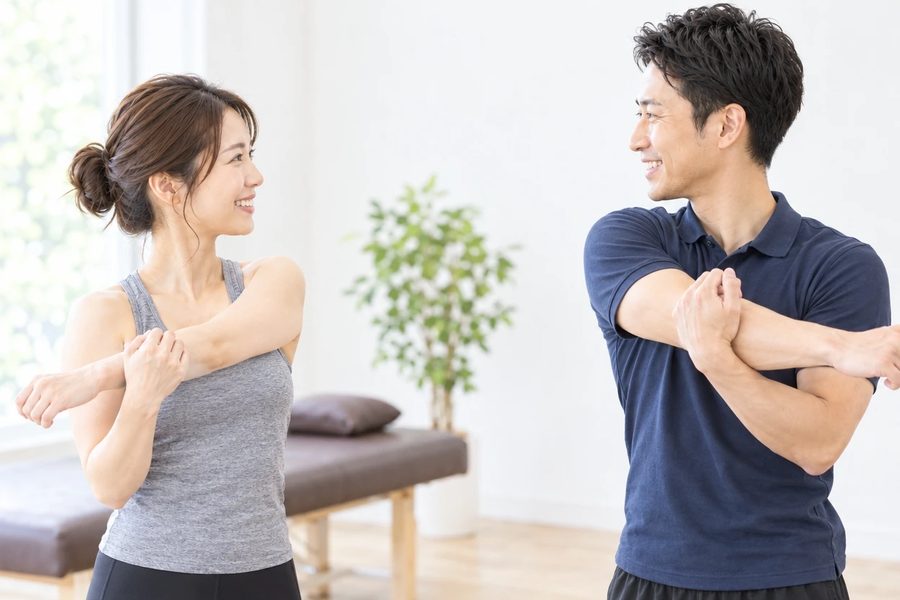 トレーナーが自宅でできるセルフストレッチを実演し、女性が真似している様子